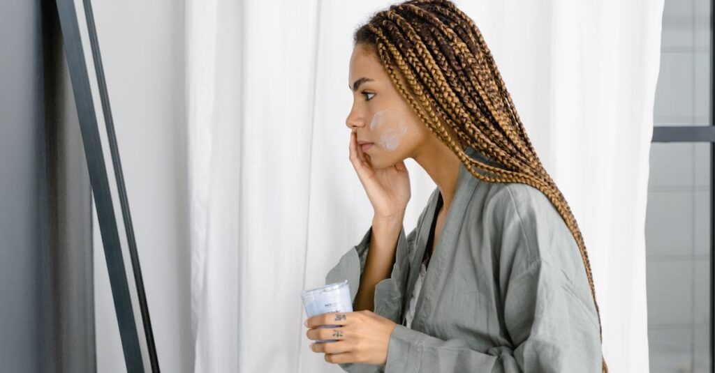 Young woman in robe applying moisturizer in front of mirror as part of her daily skincare routine.