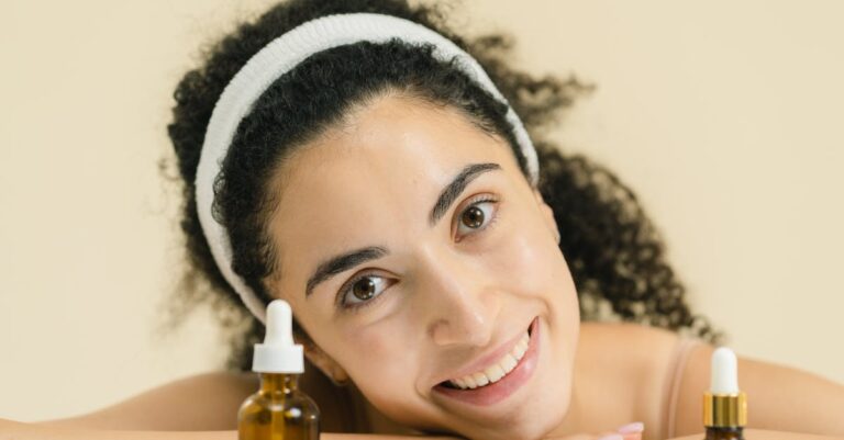 Woman with curly hair smiling, showcasing skincare products, indoors.